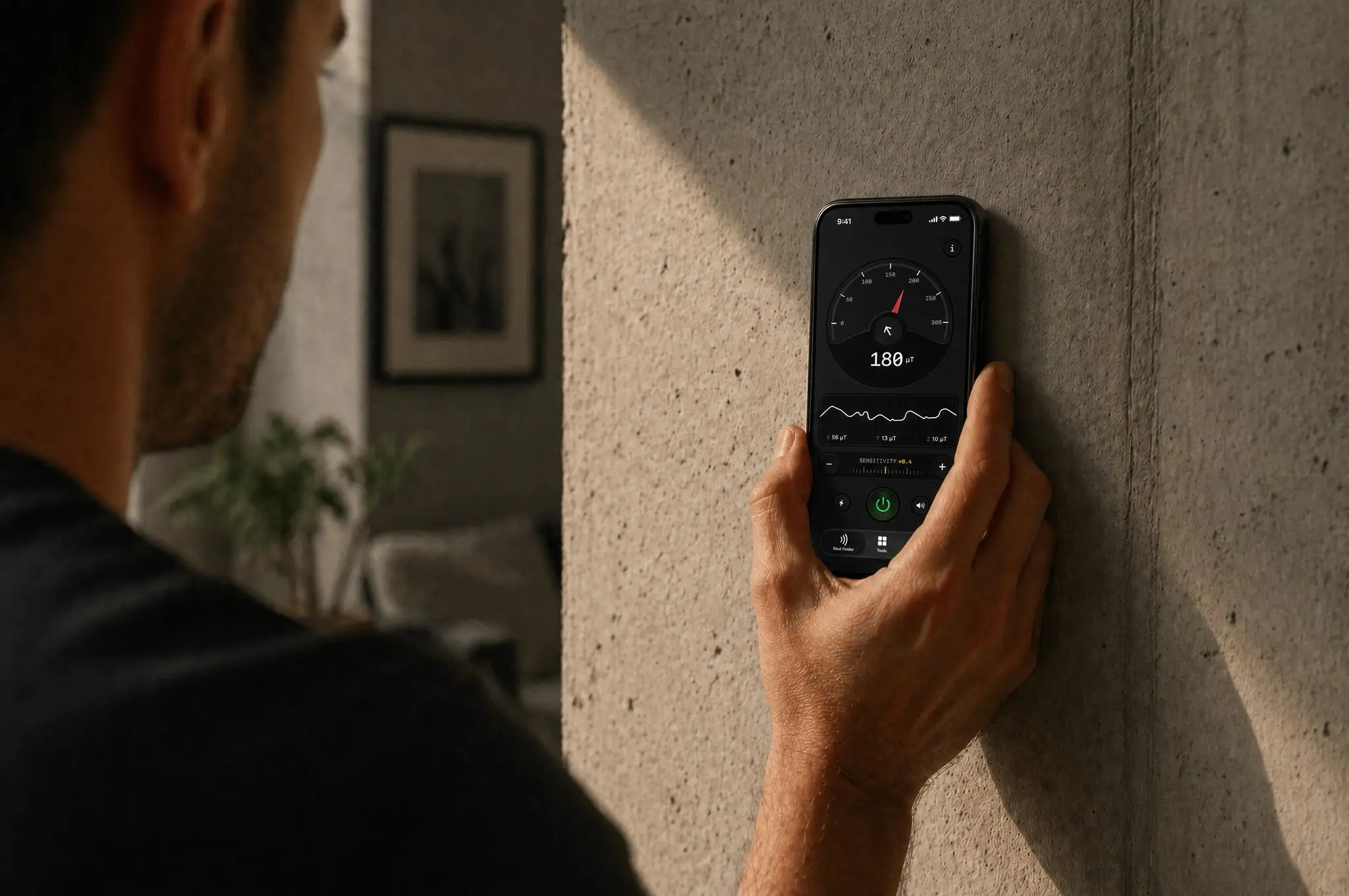 Hand sliding an iPhone across a drywall surface to scan for studs