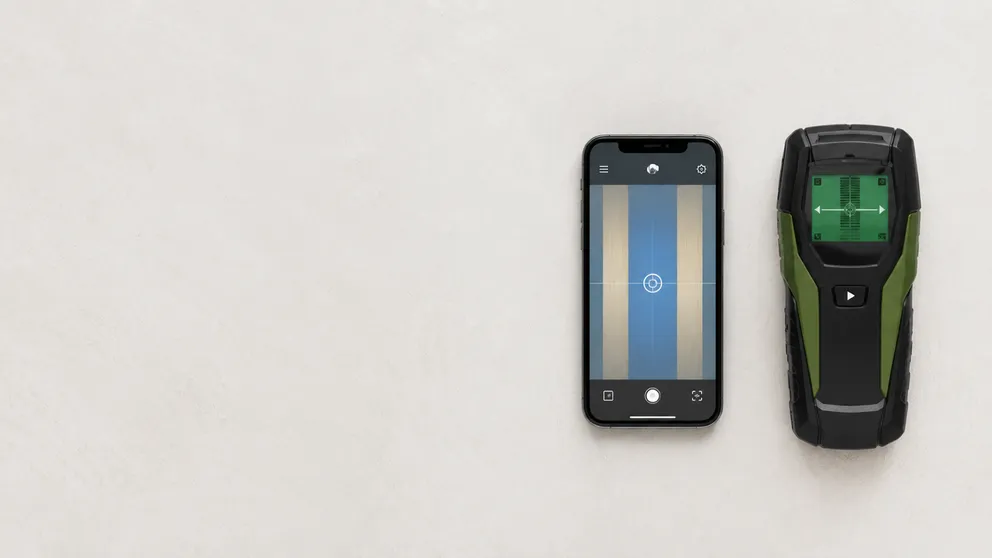 A smartphone stud finder app next to a Walabot-style wall imaging device on a table